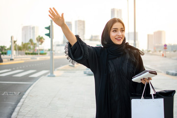 Beautiful muslim woman with shopping bags, phone and wallet hitching a taxi on the street