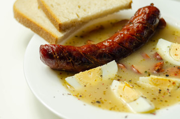 Traditional polish sour soup with sausage and eggs in ceramic bowl