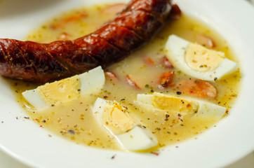 Traditional polish sour soup with sausage and eggs in ceramic bowl