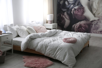 Fototapeta na wymiar Comfortable bed near wall with floral wallpaper. Stylish room interior