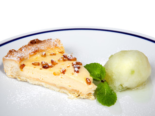 Piece of cheesecake with pine nuts, mint and frozen juice on white plate