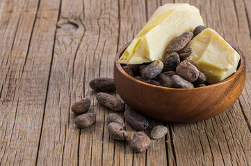 Cocoa butter or Cocoa bean solid oil with raw cocoa beans on wooden rustic backdrop, healthy natural oil