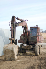 An old excavator stands at the fence of a construction site.
