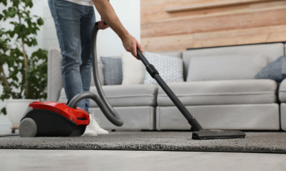 Young man using vacuum cleaner at home, closeup - obrazy, fototapety, plakaty