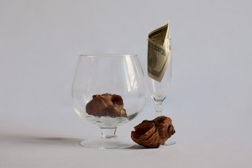 Two glasses are on the table. In one glass a shell in another glass a dollar bill