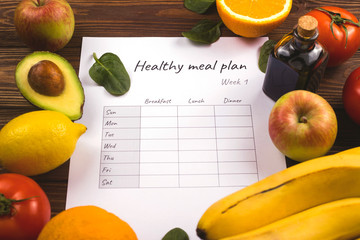 Healthy weekly meal plan among fresh organic fruits and vegetables cooking ingredients on wooden table.