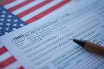 Obraz premium Form 1040 U.S. Individual Income Tax return next to flag of USA. Close up view.