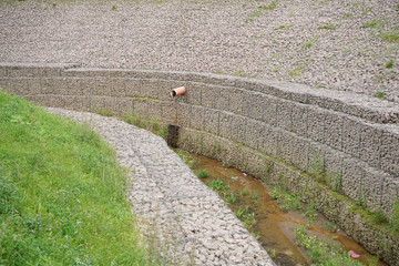 Fototapeta na wymiar a newly made stream in the middle of the city in stone banks of small stones in an iron grid. the stream is dry, waiting for water to fill .