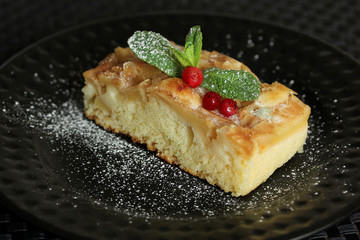 Desserts. Apple biscuit cake with fresh cranberries and mint, topped with powdered sugar on a black plate. Background image, copy space