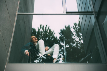 Young woman alone and depressed in a wheelchair looking out the window. Disabled woman in shock,...
