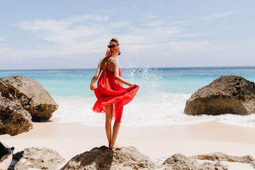 Photo from back of shapely tanned girl standing on big stone. Outdoor shot of graceful female model...