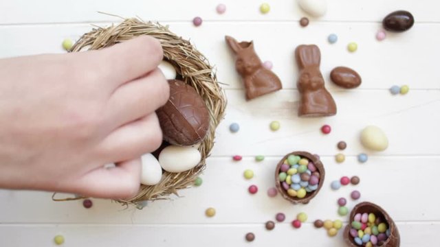 Top view of woman hand putting chocolate eggs and easter sweets on wooden table