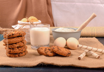 Cup of milk with cinnamon biscuits and flour on tablecloth