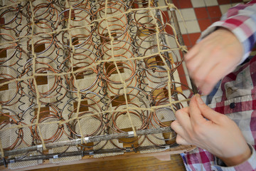 Upholstery springs. Upholstery worker tying old srpings. Upholstery workshop. Old chair springs restoration. Woman working. Hand and string.