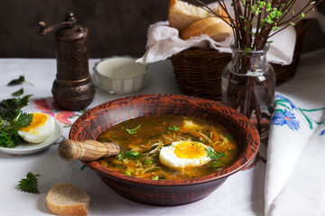 Spring green soup with herbs, vegetables and green peas, served with egg and sour cream. Rustic style.