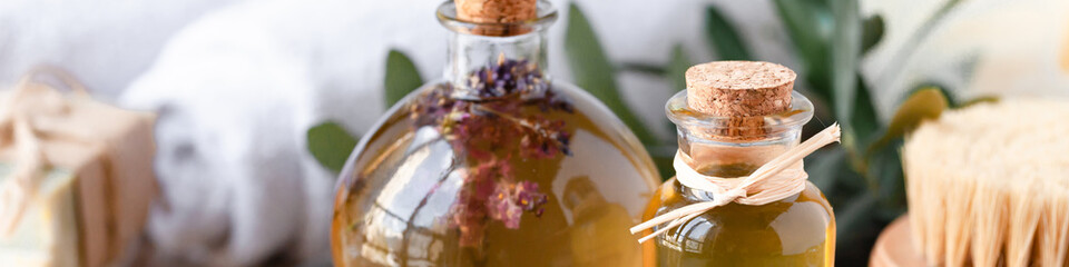 Concept of natural ingredients in cosmetology for gentle skin care. Organic olive oil in glass bottle, handmade soap bars. Atmosphere of serenity and relax. Rustic wooden background, banner format