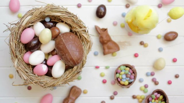 Hands taking almonds and chocolate eggs from table decorated with Easter candy. Top view