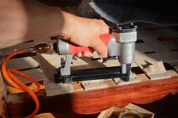 Making new upholstery on old restored furniture. Woman work with pneumatic stapler in upholstery...