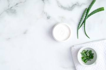 Cosmetic cream jar and green sliced stems aloe vera on marble background. Organic moisturizer hand cream. Hand skin care and beauty treatment concept