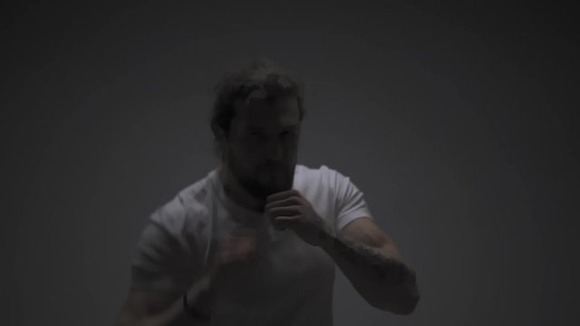 Fitness man fighting with camera indoor workout. Close up male athlete doing warm up exercises isolated on white with dark lights tone. Sportsman fighting on camera in slow motion.