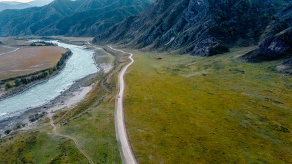 The road next to the river along the mountain ranges. Mountain landscape aerial view from a drone. Altai