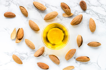 Almond oil and nuts on a white marble background. The concept of healthy vegan food and natural cosmetics. Flat lay.