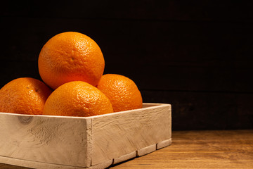 Ripe orange fruits in a crate on a wooden surface background