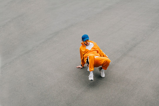 Street dancer in tracksuit dancing hip hop on asphalt, top view, isolated. Stylish young man. in bright casual clothes dancing a dance dance on a background of gray asphalt. Copy space - Powered by Adobe