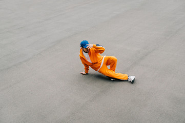 Stylish street dancer training hip hop dance and paved playground, top view, isolated. Fashionable man in an orange tracksuit dancing breakdance on the asphalt fondue. Background