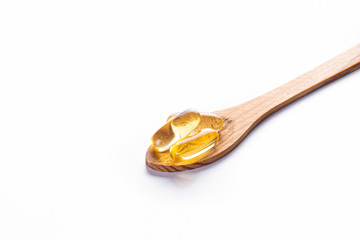 Pile of omega 3 fish liver oil capsules in wooden spoon. Big golden translucent pills on isolated background. Healthy daily fatty acids nutritional supplement. Top view, flat lay, copy space, close up