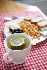 green tea with lemon with breakfast set of fried egss with lentils, olives, blue cheese on a background