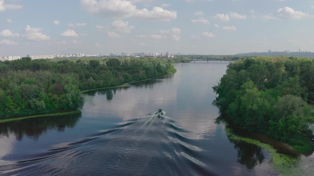 sunny summer day over green islands on a river in a northern city, people actively spend time on the river, wake boarding, wake surfing after fast boats - Aerial Fligh