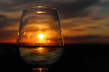 Glass with white wine on beautiful sunset background, sun and sky are reflected in alcohol drink. Concept of celebration, evening party at resort, romantic dinner outdoors