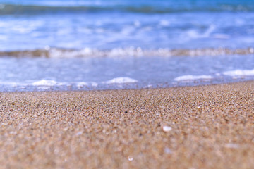 Waves with foam close up on a tropical sandy beach on a sunset. Copy space for background