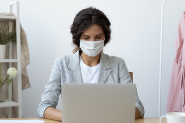 Fototapeta na wymiar Young business woman wearing face mask working on computer seated at workplace desk in office room protecting herself from getting grippe vs COVID-19 corona virus pandemic infectious disease concept