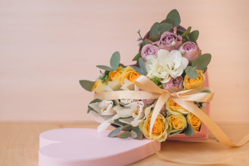 Stylish flowers arrangement in a pink hatbox. White orchid, purple and yellow roses with bunch. Birthday present. Flowers bouquet on background whith copy spase. Romantic concept