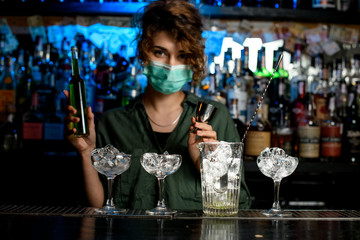 bartender girl in medical mask preparing to make mixture.