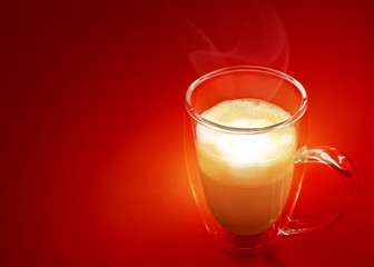 Hot coffee with milk in a glass with double walls isolated on red background. Latte, cappuccino