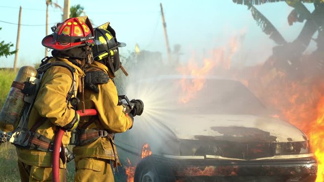 firefighter using spraying water to the fire buring in car accident
