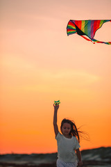 Little girl flying a kite on the beach with turquiose water