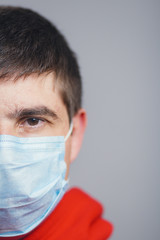 half of head of serious young man face wearing protective medical mask on a gray studio background, concept of desease and quarantine measures,coronavirus spread in Europe