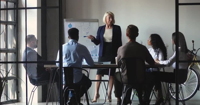 Confident mature international company leader explaining developing strategy to motivated executives on brainstorming meeting in office. Focused diverse business people listening to older partner.