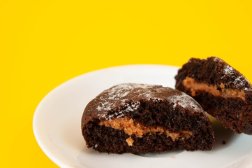 dark brown cookies on a white plate, on a bright yellow background, mouth-watering photo, place for text. Minimal concepts. Tasty almond cookies. Copy space.