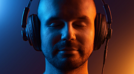 Young man in headphones enjoys the music. His eyes are closed. Two-tone lighting