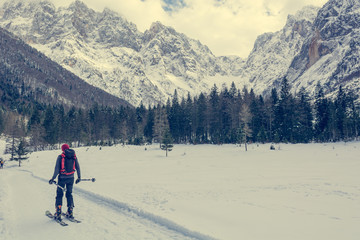 Back country skier skiing across snow covered meadow surrounded with mountains.