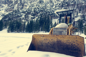 Old bulldozer parked on snowy meadow covered with snow.