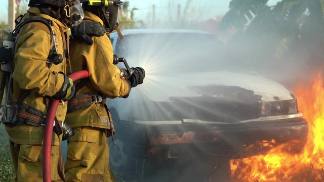 firefighter using spraying water to the fire buring in car accident

