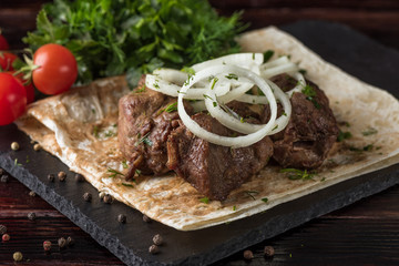 Shish kebabs with vegetables and pita bread on a slate tray in a dark key
