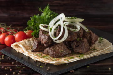 Shish kebabs with vegetables and pita bread on a slate tray in a dark key