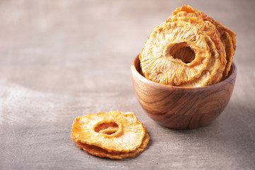 Slices of dried pineapple in wooden bowl on wood textured background. Copy space. Superfood, vegan, vegetarian food concept. Macro of pineapple texture, selective focus. Healthy snack